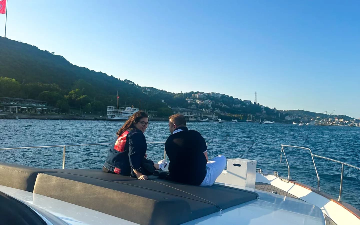 Luxury private yacht cruising through the Bosphorus strait in Istanbul with Ottoman palaces and suspension bridge in the background