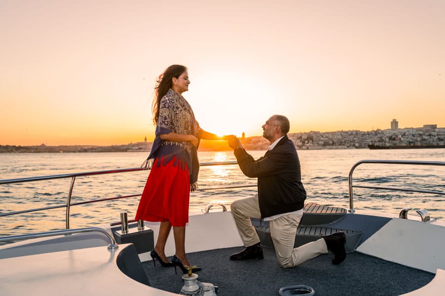 Ein Mann kniet bei Sonnenuntergang auf dem Deck einer Yacht für einen Heiratsantrag