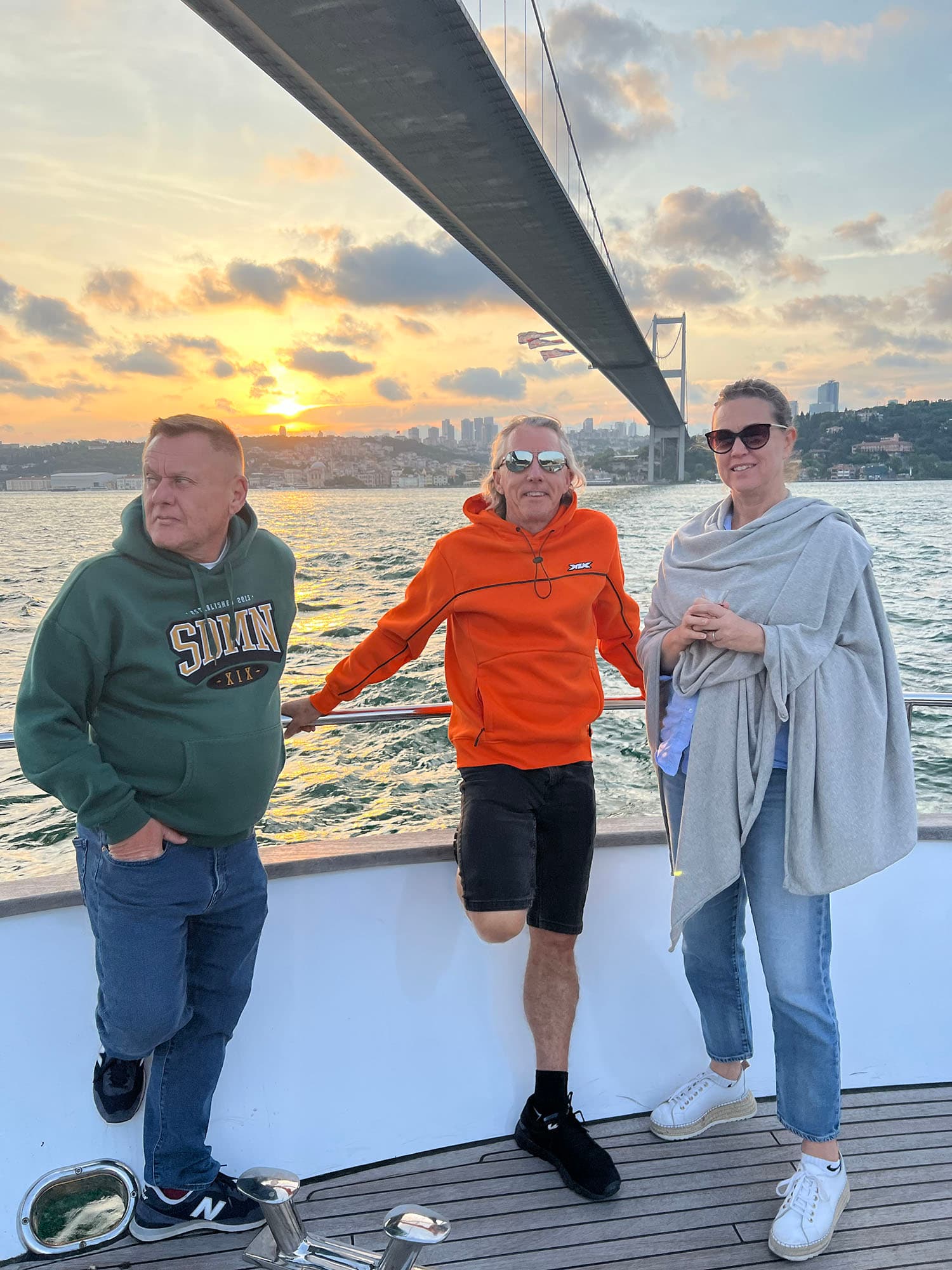Three guests on deck below the Bosphorus Bridge at sunset