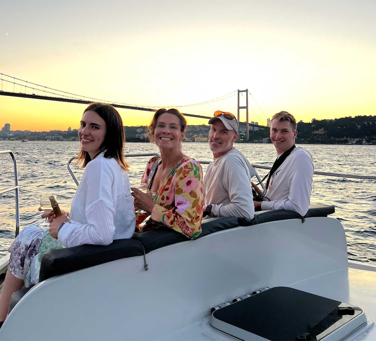Four friends sitting on the bow with the bridge behind them at sunset