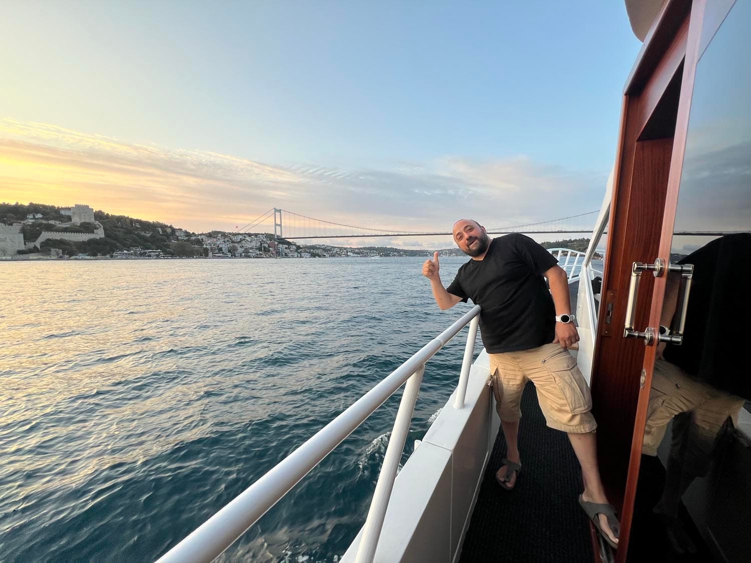 Ospite a bordo al tramonto, con la fortezza di Rumeli Hisarı e un ponte sul Bosforo sullo sfondo