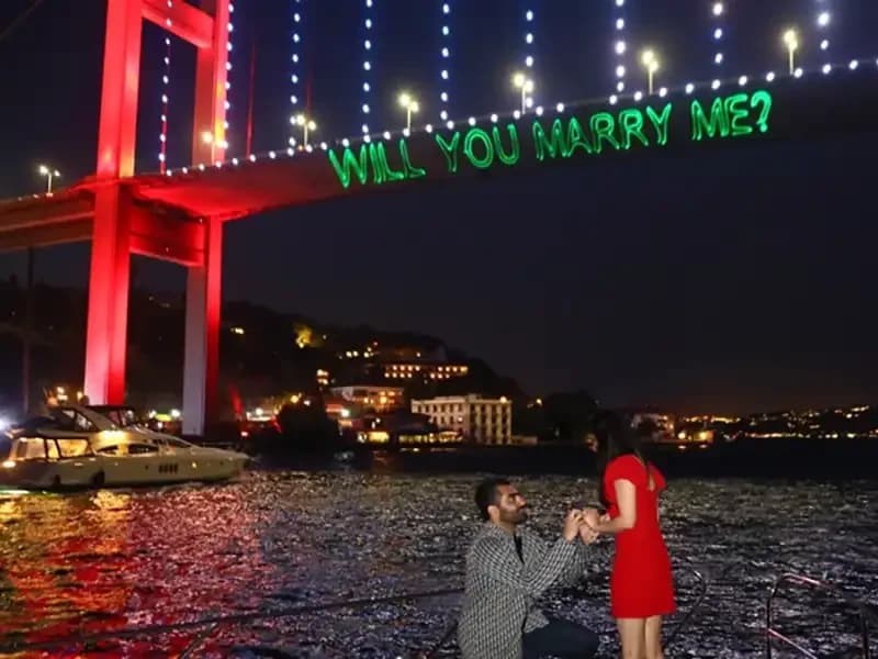 A proposal at night beneath the lit Bosphorus Bridge